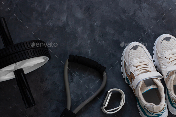 Sport equipment flatlay composition, white sneakers,sports watch,fitness chest expander, ab wheel