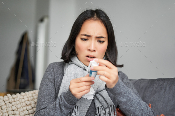 Ill korean woman looking at thermometer with concerned face, catching cold, having fever, having