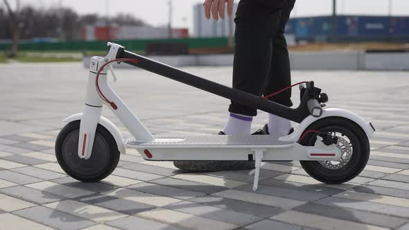 An Unrecognizable Man is Carrying an Electric Scooter alt
