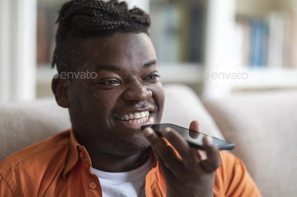 Closeup of happy black man recording voice mail on smartphone