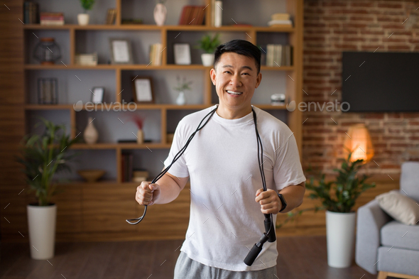 Excited asian middle aged man standing with skipping rope hang around his neck, ready to training at