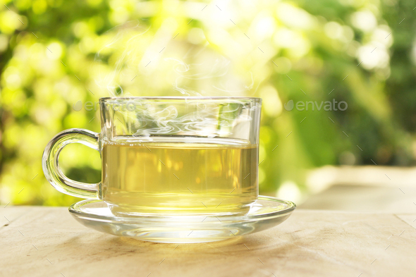Cup of hot tea with smoke on a blurred background of nature.