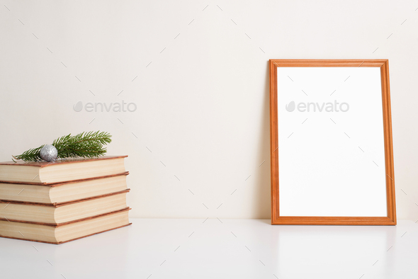 Wooden vertical picture frame mock-up. Books, pine twig, christmas ball and blank portrait frame