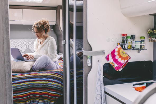 Alternative office workplace concept. Woman working on laptop in camper van bedroom. Van life