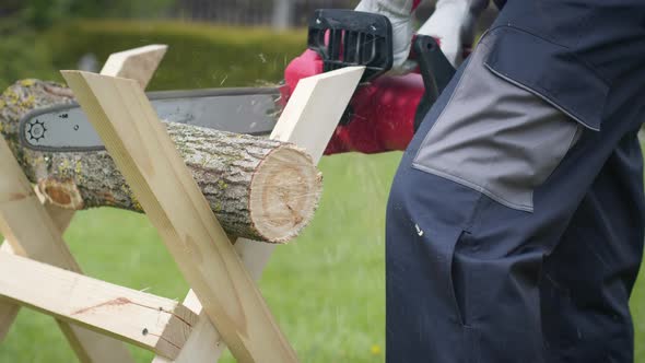 Caucasian Man in Gloves Saws Firewood with Electric Saw at Home Site. Close-up alt