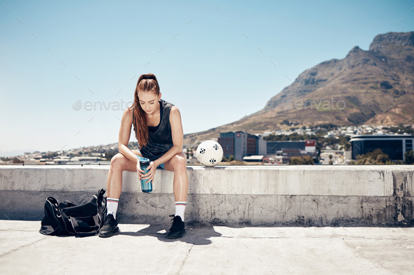 Sports athlete, woman rest on rooftop and water break after rooftop soccer training with a ball for