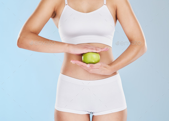 Health, weight loss and apple on stomach of woman in underwear for nutrition, diet and vegan lifest