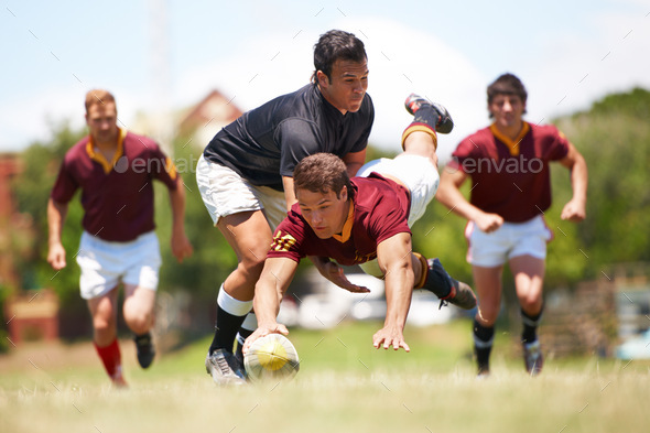 Full length shot of a young rugby player scoring a try mid tackle
