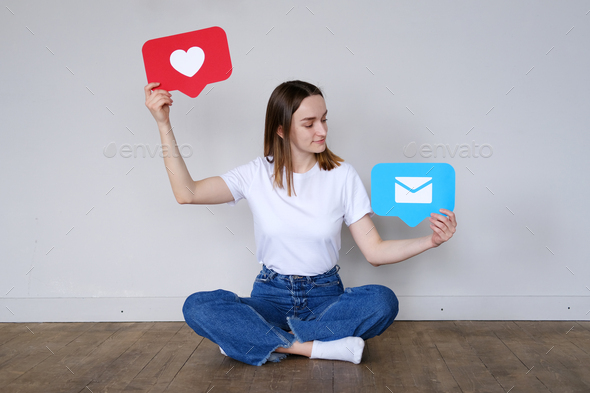 Beautiful caucasian girl sits on the floor and holds a like button and a message button