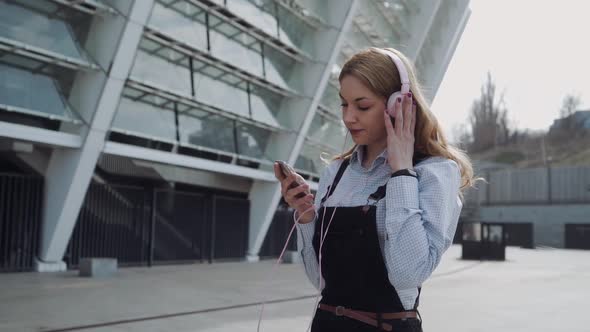 Young Woman Listens Music on Headphones with Music Application at the Street alt