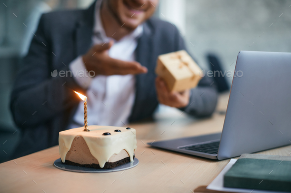 Close up of Birthday cake with businessman making video call in the background.