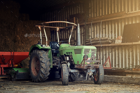 No farm is complete without one. Shot of a rusty old tractor standing in an empty barn.