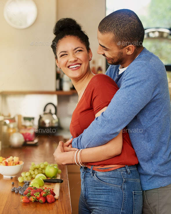 Shot Of A Young Man Hugging His Wife While She Prepares A Healthy Snack