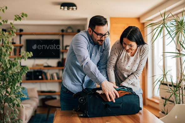 Couple trying to close suitcase with too much clothes.