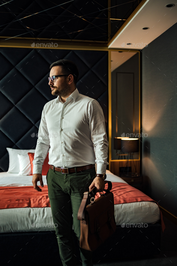 Portrait of a handsome businessman with document case standing in a hotel room. - Stock Photo - Images