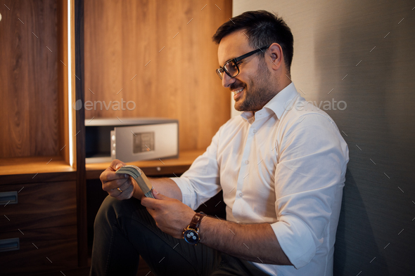 Side portrait of a smiling man with stack of cash money near the small safe deposit box.