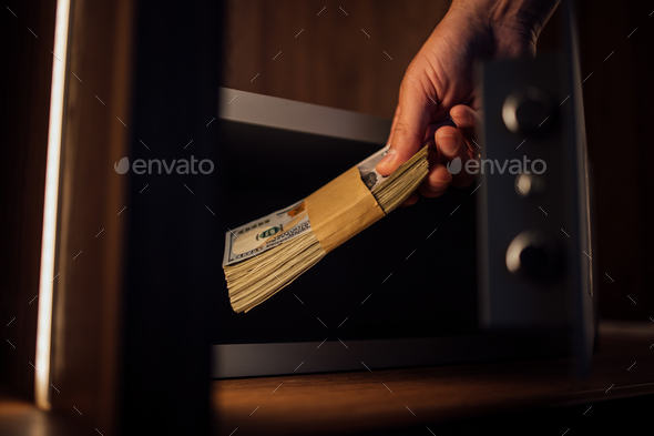 Close-up image of male hand keeping dollar banknotes in a safe deposit box.
