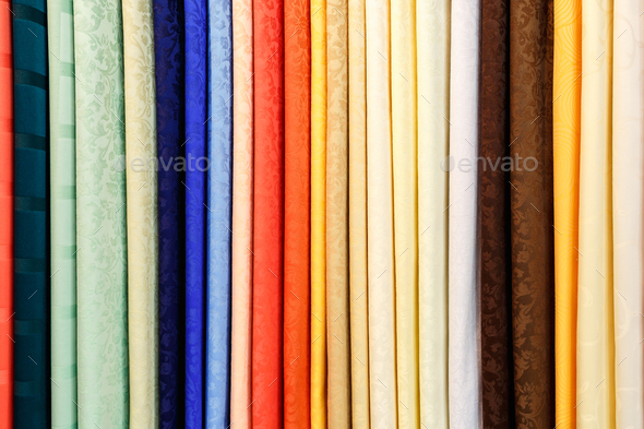 wide selection of different color textile silk fabrics clothes lay in row in drapery store