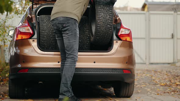 A Man Unloads Winter Tires From a Car Trunk alt