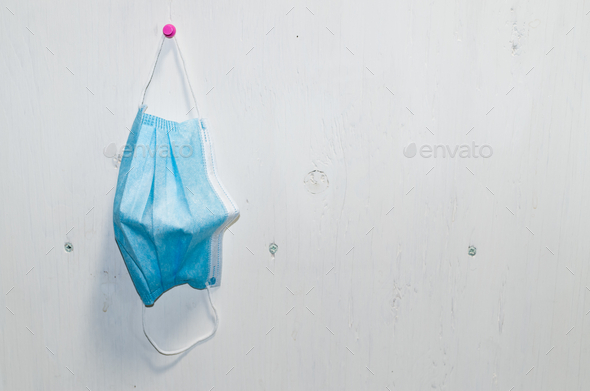 Closeup of a used disposable mask hanging on a white wall - precaution, disease control concept