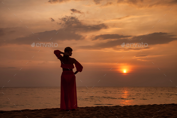 Silhouette middle aged woman arms raised standing on tropical sea sunset. Female relaxing on beach