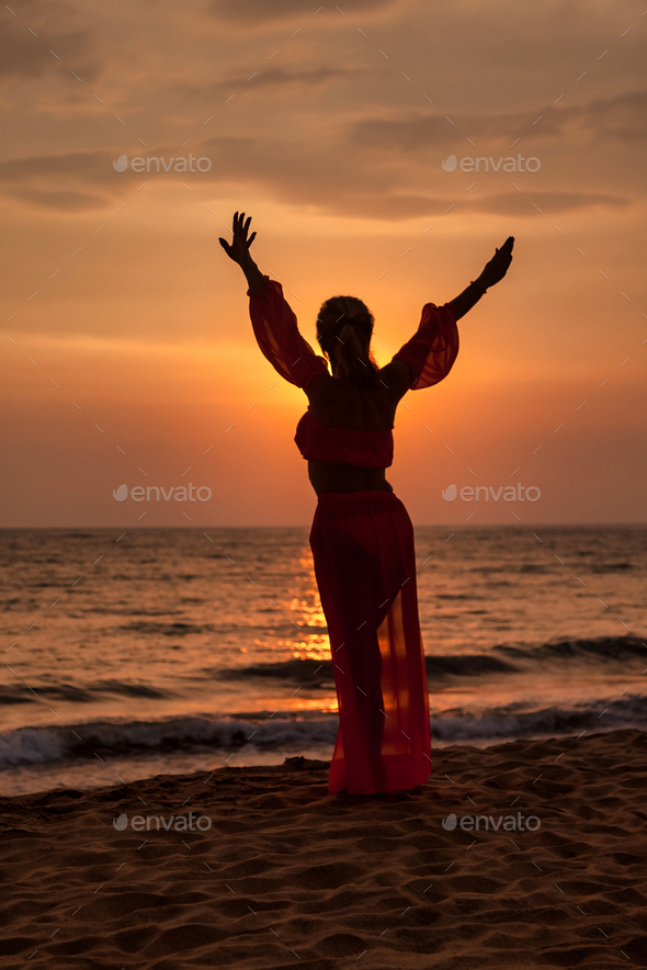Silhouette middle aged woman arms raised on tropical sea sunset. Female posing relaxing on beach