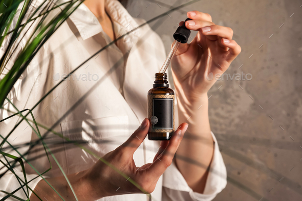 Lady hands holding pipette and massage or cosmetics oil bottle for applying drops to skin or hair
