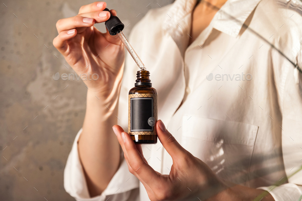 Young lady hands holding pipette and massage or cosmetics oil bottle for applying drops to skin