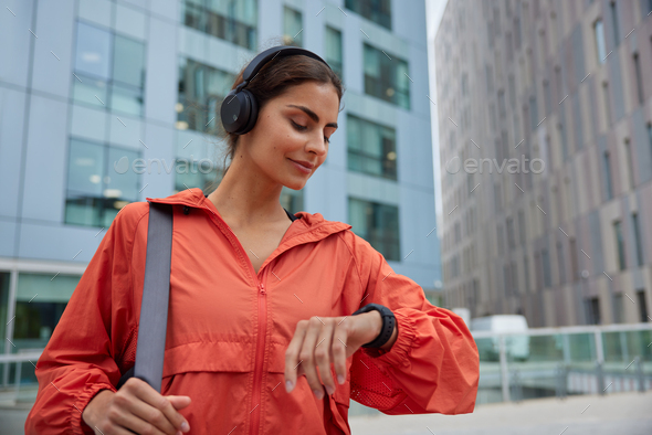 Female runner looks at smartwatch while going for run checks time listens music via headphones dress