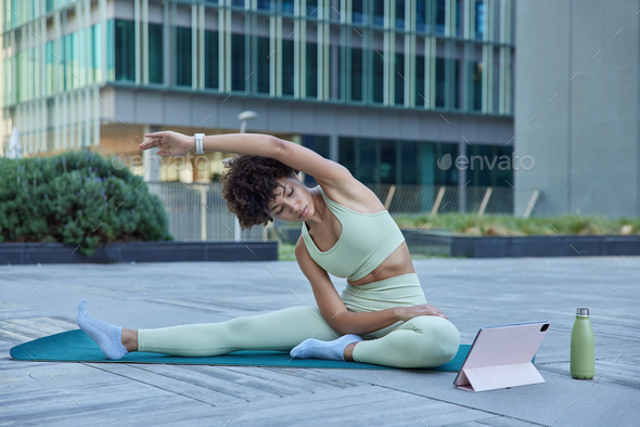 Flexible slim woman in tracksuit exercises yoga poses at karemat watches  instructional videos on tab Stock Photo by wayhomestudioo