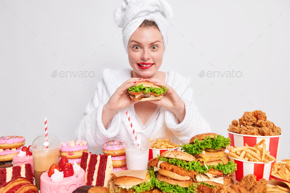 Hungry woman eats greedily burger likes cheat meal and unhealthy junk food has overeating habit wear