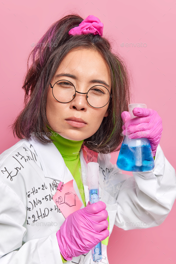 Serious female scientist conducts chemical experiment holds glass
