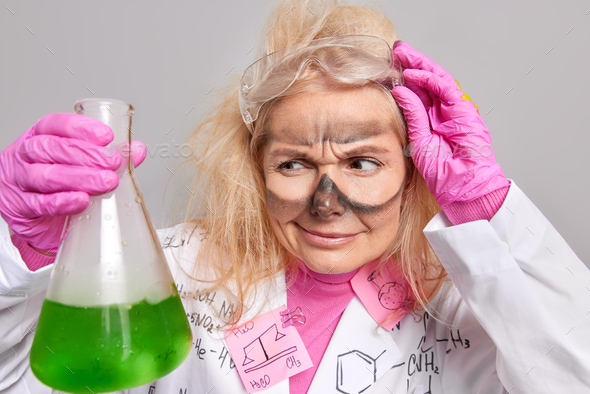 Scientific discovery and chemisty concept. Serious female chemist looks attentively at beaker with g