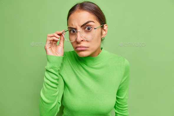 Serious confident woman looks attentively through transparent glasses wears casual turtleneck has de