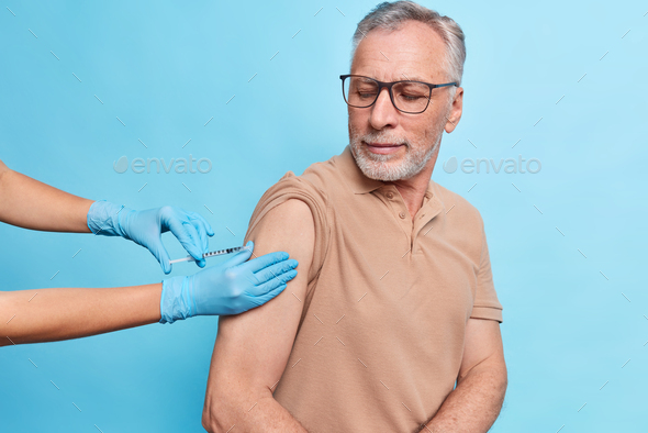 General practitioner vaccinates old male model gives injection against coronavirus. Bearded mature m