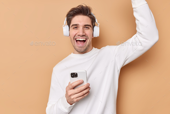 Glad cheerful man dances and laughs happily enjoys favorite playlist listens music via headphones ho - Stock Photo - Images