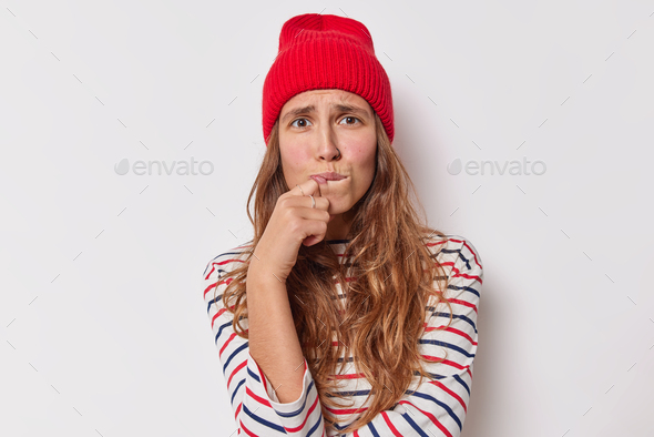 Nervous young long haired woman bites lips being fraid of something feels sorry for doing wrong thin