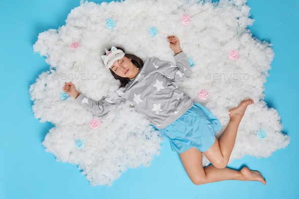 Overhead shot of relaxed young Asian woman stretches arms while sleeping has deep healthy sleep dres