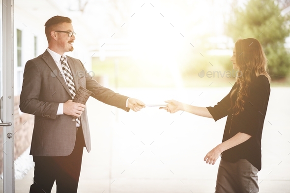 Male and female church members exchanging notes at church doors with bright sunlight in background
