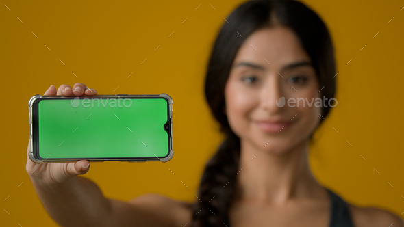 Close up Indian ethnic smiling woman female girl in yellow studio holding phone horizontal showing