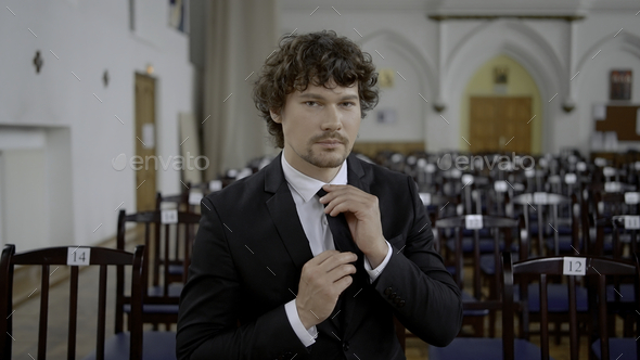 Young man with curly hair in black and white classic suit in empty church. Action. Groom prepared