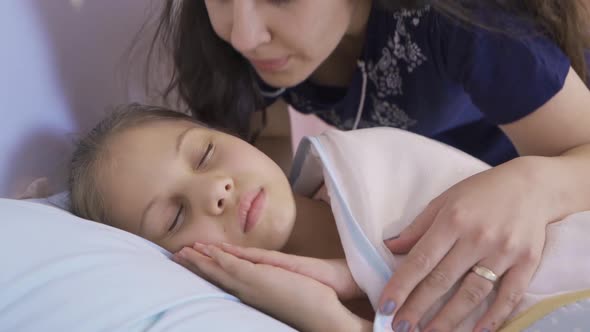 The mother, straightening her daughter's blanket, kisses her cheek. alt