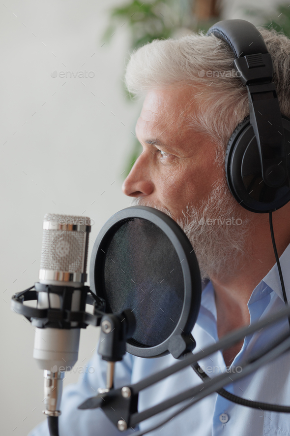 older man with gray hair irecording podcast in recording studio with microphone and headphones