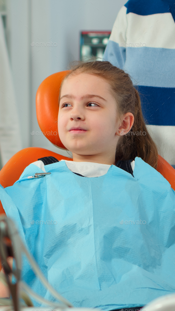 Close up of kid patient with toothache wearing dental bib talking with dentist