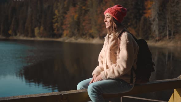 Portrait of Inspired Beautiful Smiling Woman Hiker Backpacker Sitting on Wooden Pier at Beautiful alt