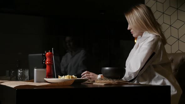 Blonde Girl in a White Shirt Eats a Dish Sitting in a Restaurant
