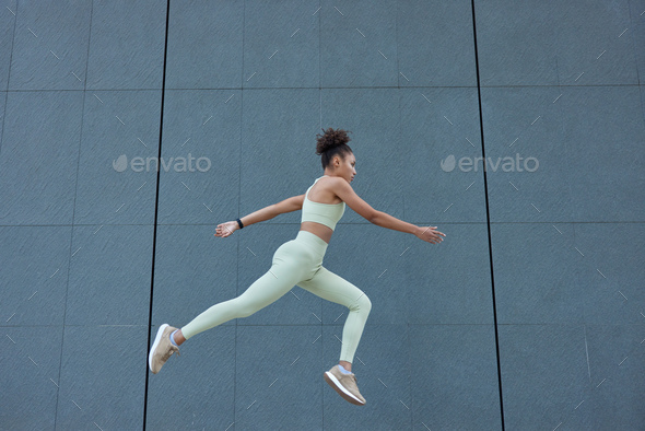 Full length shot of active slim woman jumps high in air has cardio training dressed in sportswear po