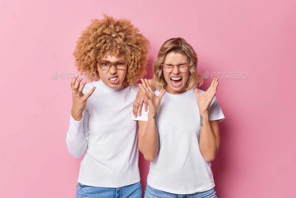 Irritated two young women friends gesture angrily feel annoyed exclaim loudly bothered with too loud