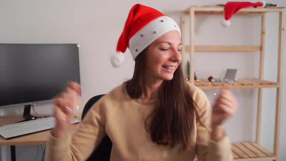 Caucasian Woman Dancing in Office with Santa Hat. Merry Alone Christmas.  alt