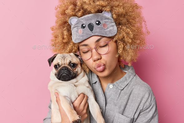 Pleased romantic curly woman keeps eyes closed and lips folded spends time with favorite pet wears b
